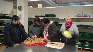 Mitarbeiterinnen stehen an einem Tisch im De-Cent-Laden und bereiten Lebensmittel vor.