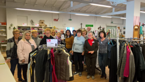 Gruppenfoto der Mitarbeiter/Mitarbeiterinnen im Sozialmarkt (zwischen Kleiderständern)